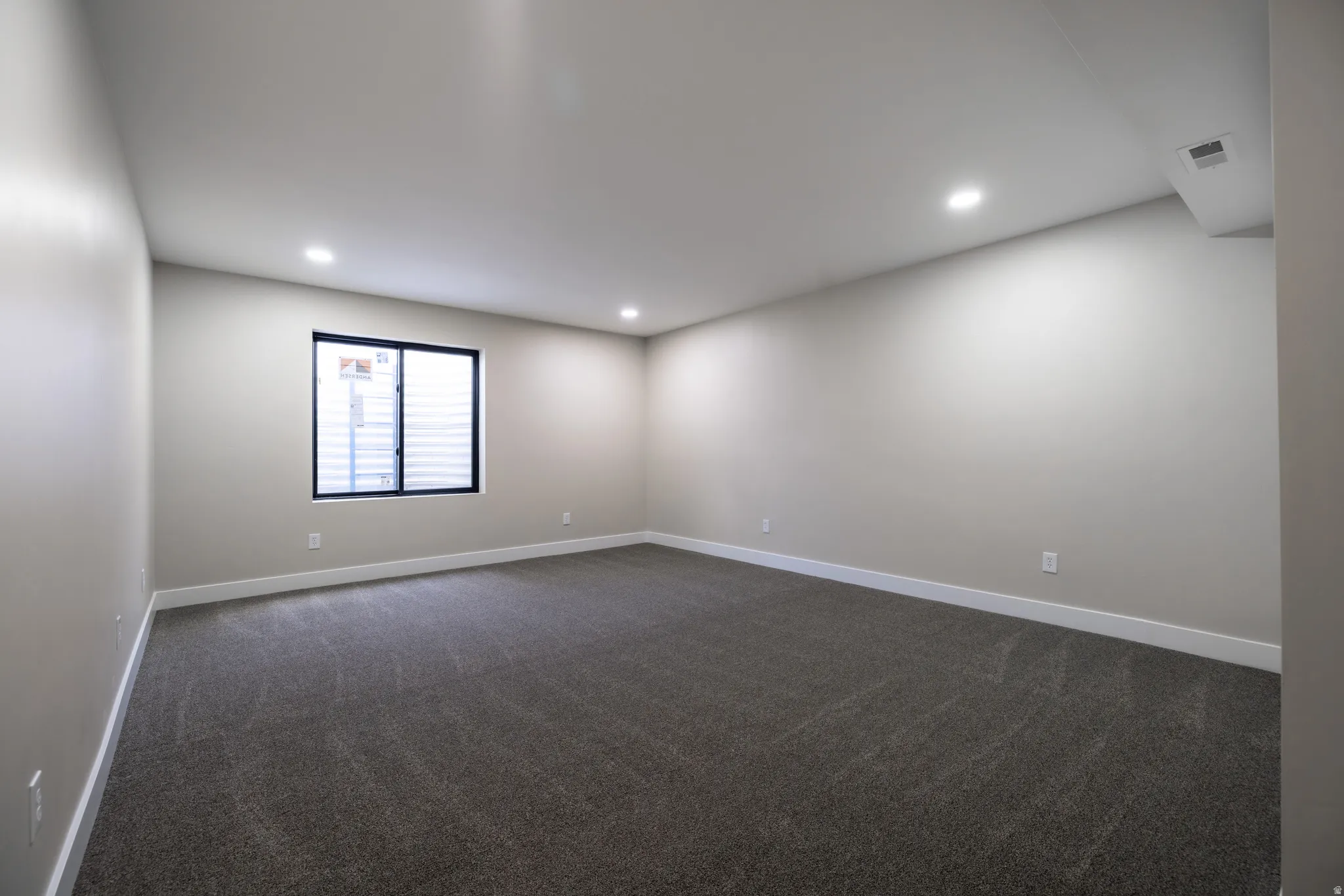 Recessed lighting, large window with blinds, light-toned walls, and dark patterned carpeting