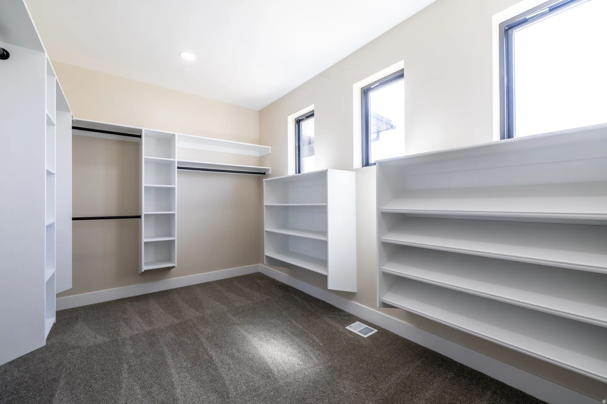 Built-in closet system with shelving and hanging rods, recessed lighting, carpet flooring, and multiple windows