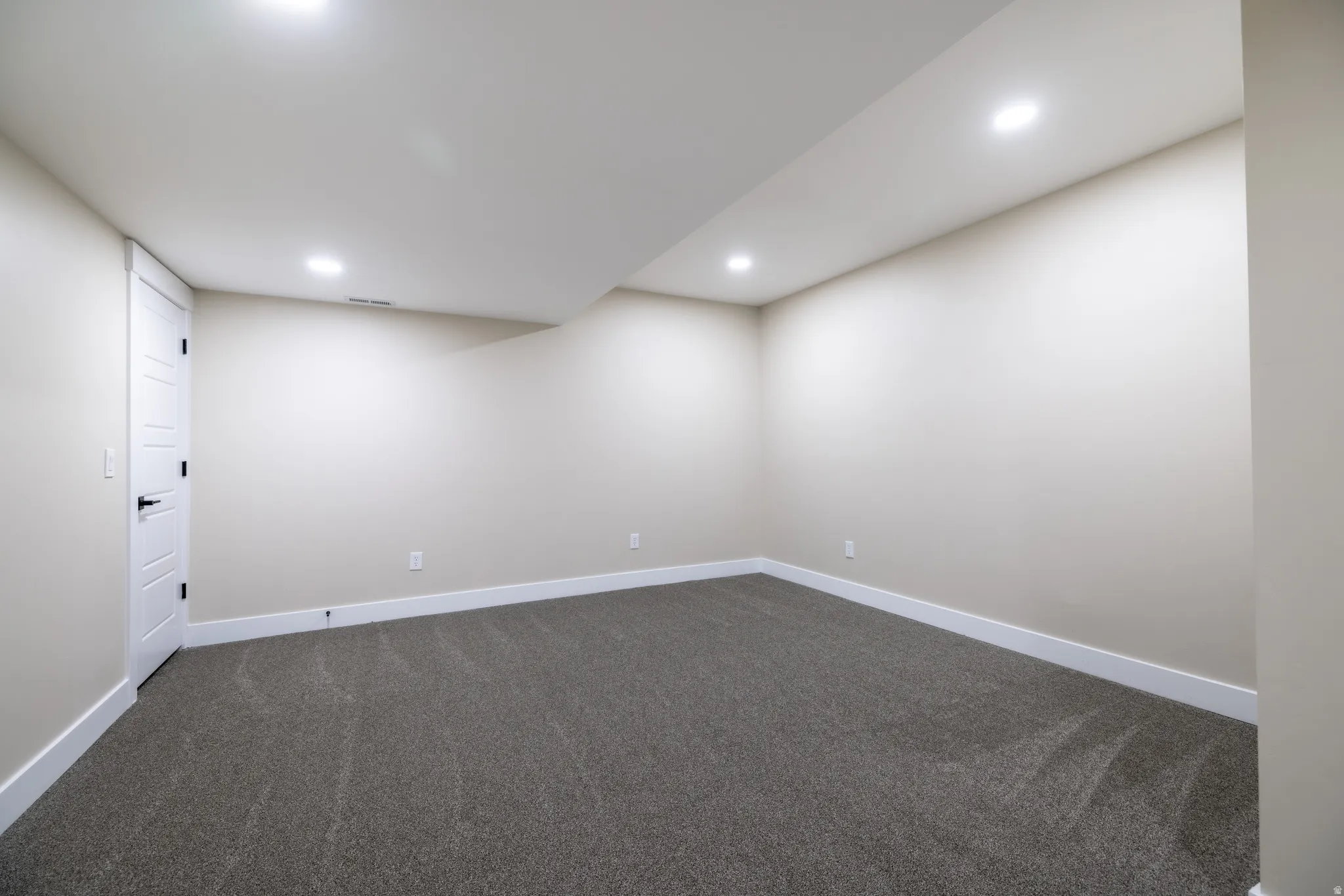 Recessed lighting, neutral wall paint, gray carpet flooring, white trim, and a white paneled door with black hardware