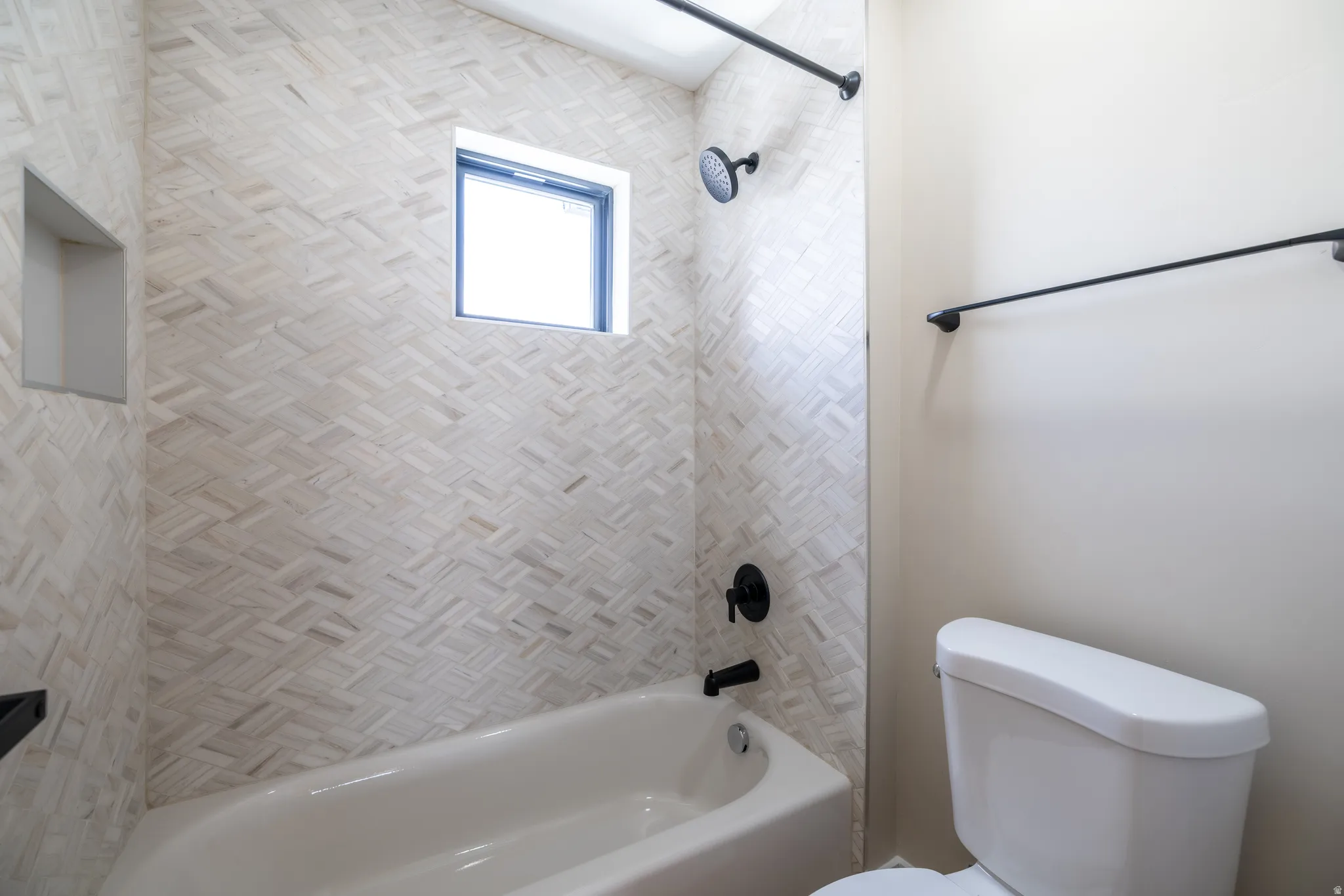 Bathtub with chevron-patterned tile surround, matte black shower fixtures, integrated shower niche, and small window