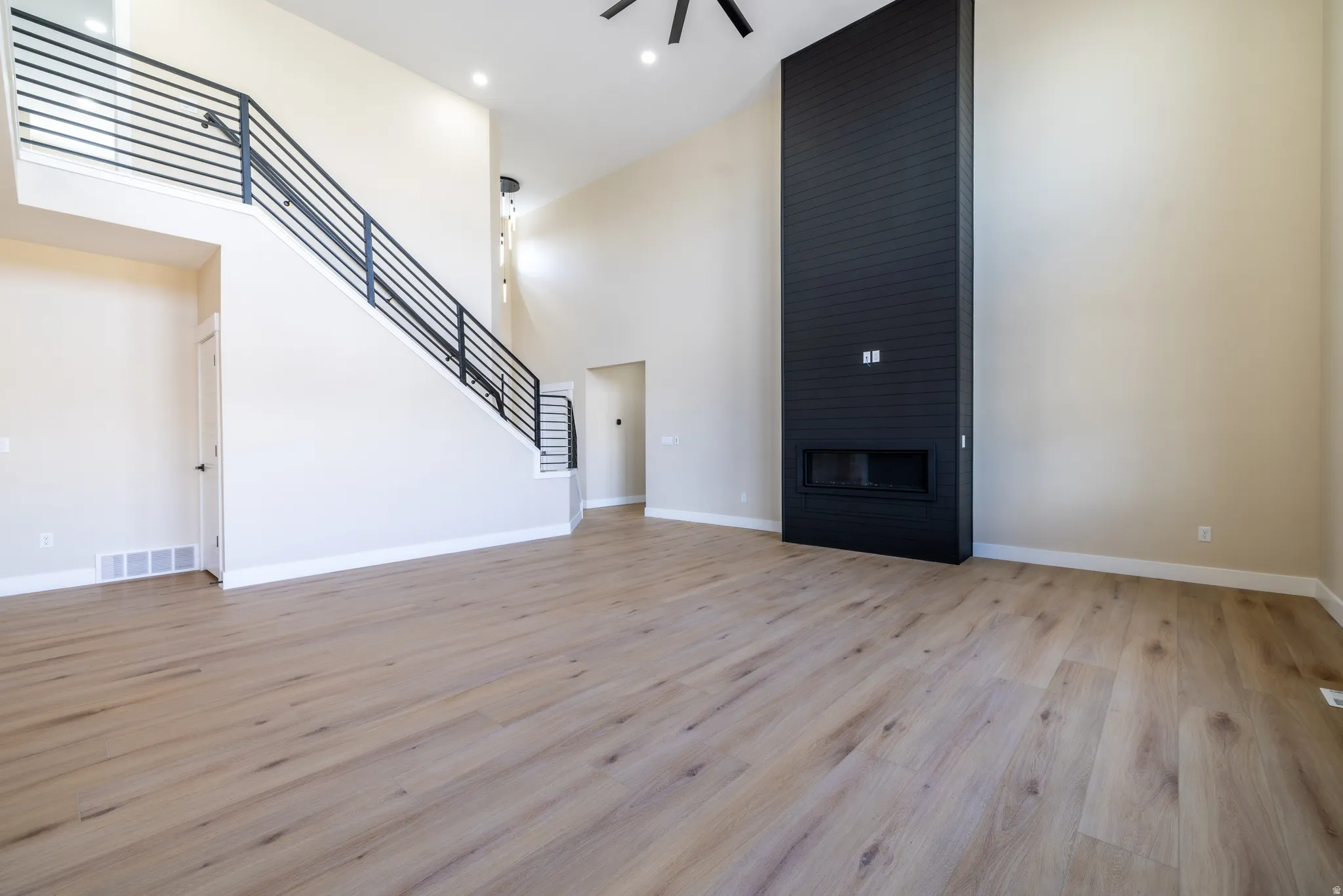 Vaulted ceilings, wood-finish flooring, a contemporary black fireplace surround, and modern black stair railings