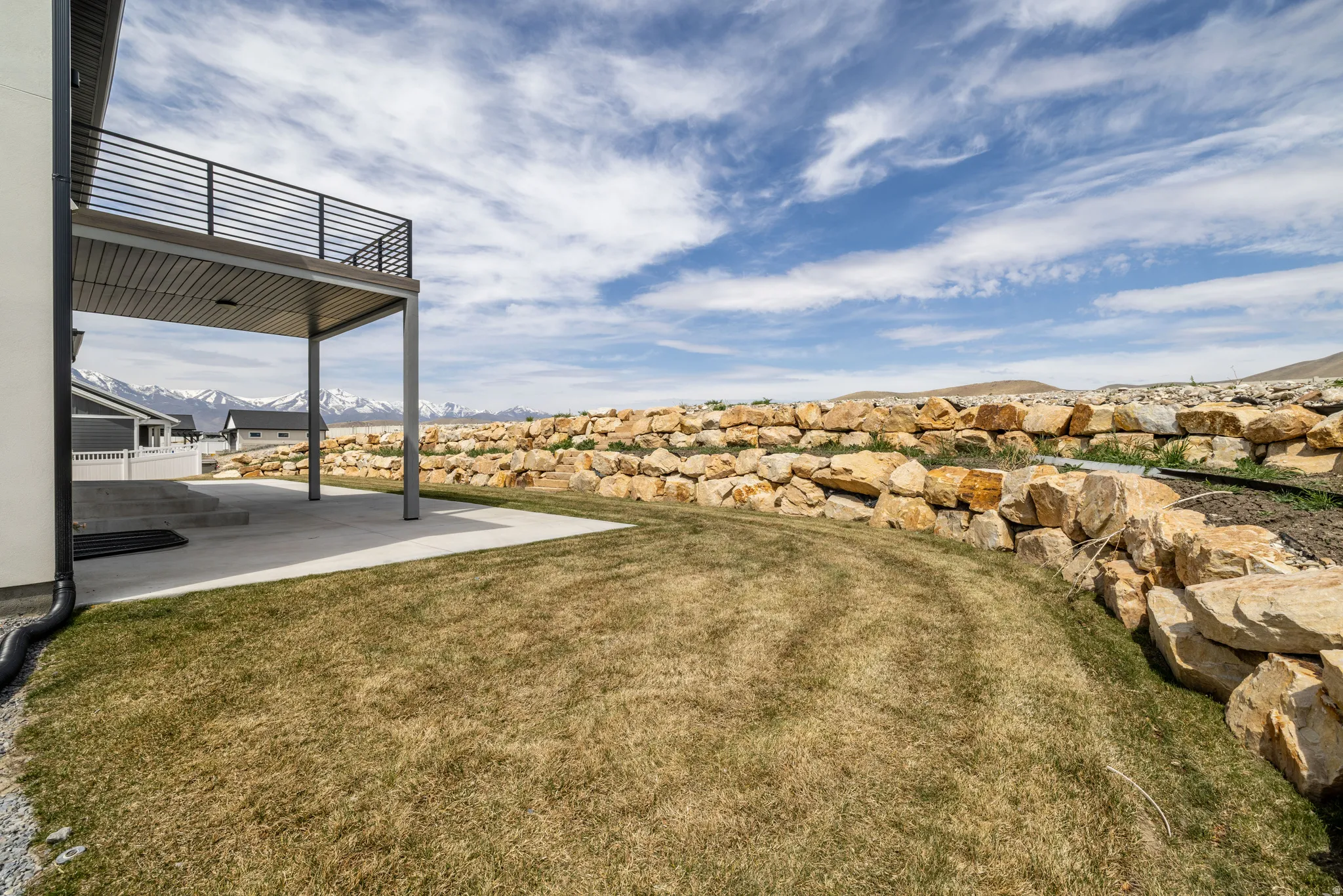 Lower concrete patio with overhead deck, metal deck railing, and rock retaining wall