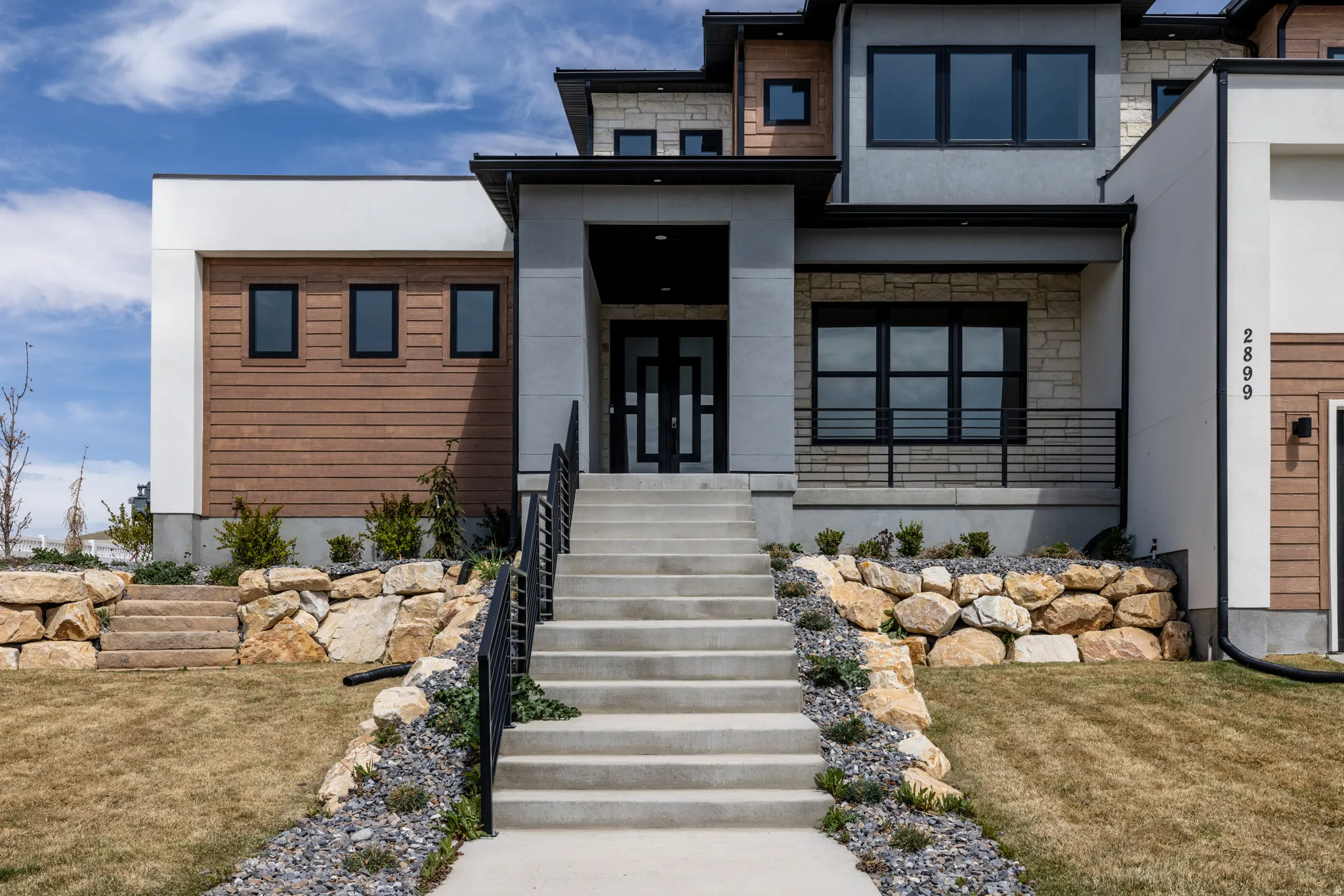 Contemporary exterior with mixed material facade, concrete stairs with black railings, stone retaining walls, and dark-framed windows