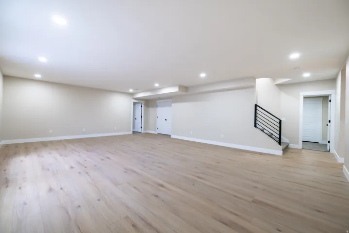 Expansive open-concept room featuring wood-finish flooring, recessed lighting, and a contemporary black metal stair railing