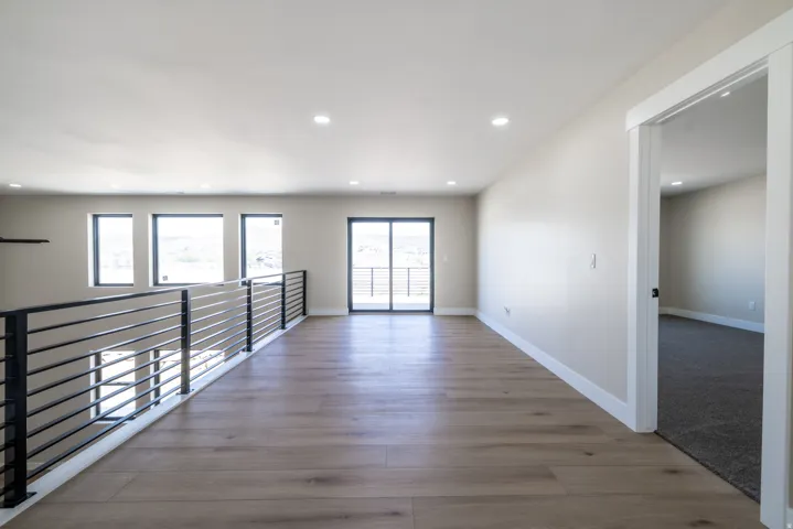 Spacious open loft area featuring wood-finish flooring, recessed lighting, and a modern horizontal metal railing