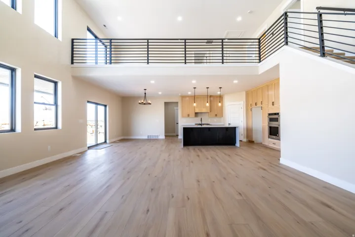 Two-story living area with high ceilings, wood-finish flooring, a modern kitchen island, light wood cabinetry, and a loft with a metal railing