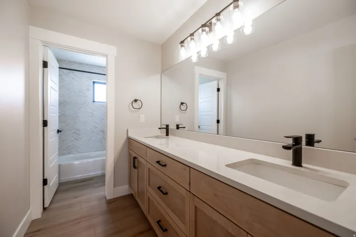 Dual vanity with integrated sinks, light wood-finish cabinetry, and matte black fixtures