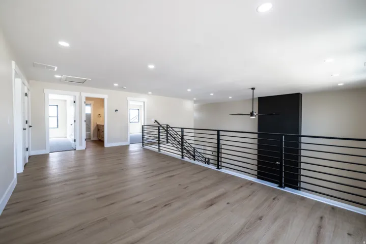 Spacious loft area featuring wood-finish flooring, recessed lighting, a contemporary ceiling fan, and black horizontal railing