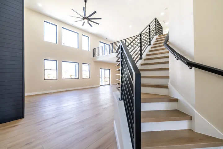 Two-story interior with wood-finish flooring, a contemporary ceiling fan, and a prominent staircase featuring black metal railings