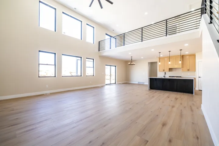 Vaulted ceilings with abundant natural light, wood-finish flooring, a kitchen island with stone countertops, and a modern horizontal railing system