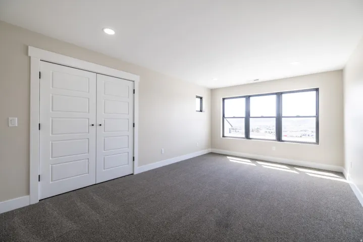 Spacious room with gray carpeting, white walls, recessed ceiling lighting, and a large multi-pane window