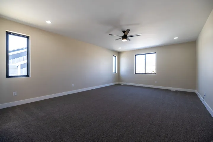 Spacious room featuring neutral-toned walls, dark carpeting, recessed lighting, a ceiling fan, and multiple windows with black trim