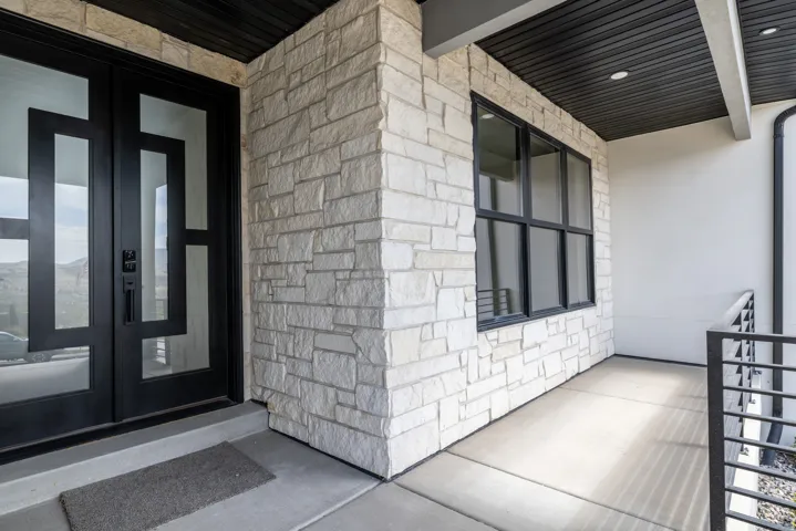 Stone veneer exterior with a concrete porch, featuring a double entry door with geometric glass panels and black-framed windows