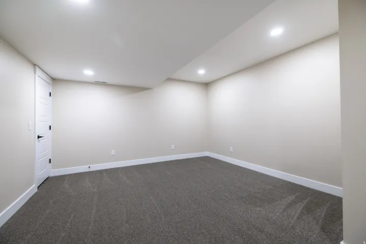 Recessed lighting, neutral wall paint, gray carpet flooring, white trim, and a white paneled door with black hardware