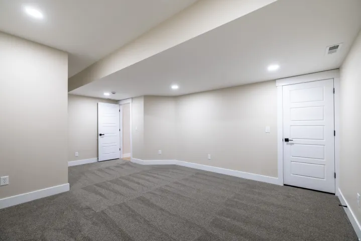Recessed lighting, neutral wall paint, gray patterned carpeting, white trim, and white paneled doors with black hardware