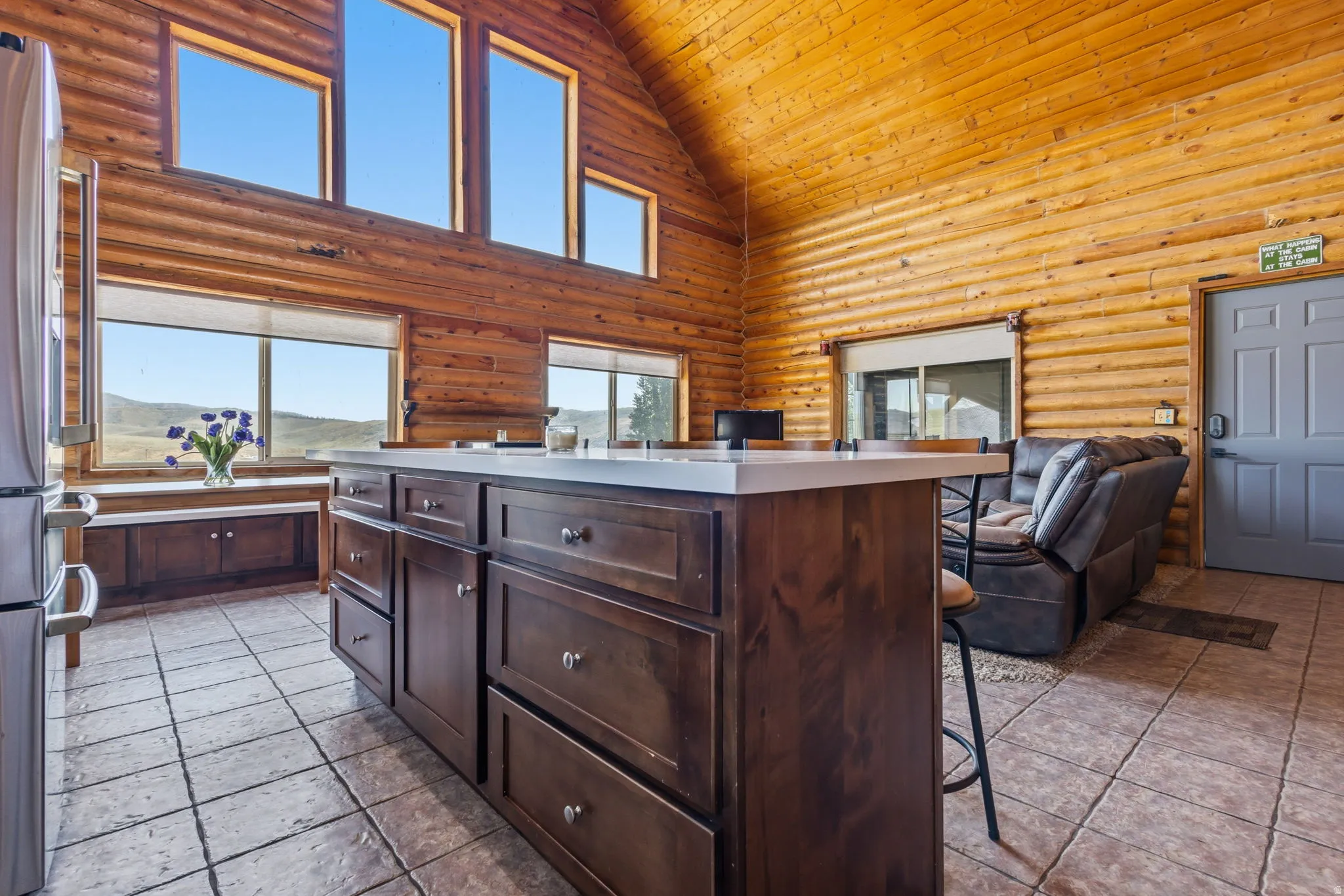 Log-style interior construction, vaulted ceiling with exposed wood, large kitchen island with built-in cabinetry, durable tile flooring, and multiple high windows