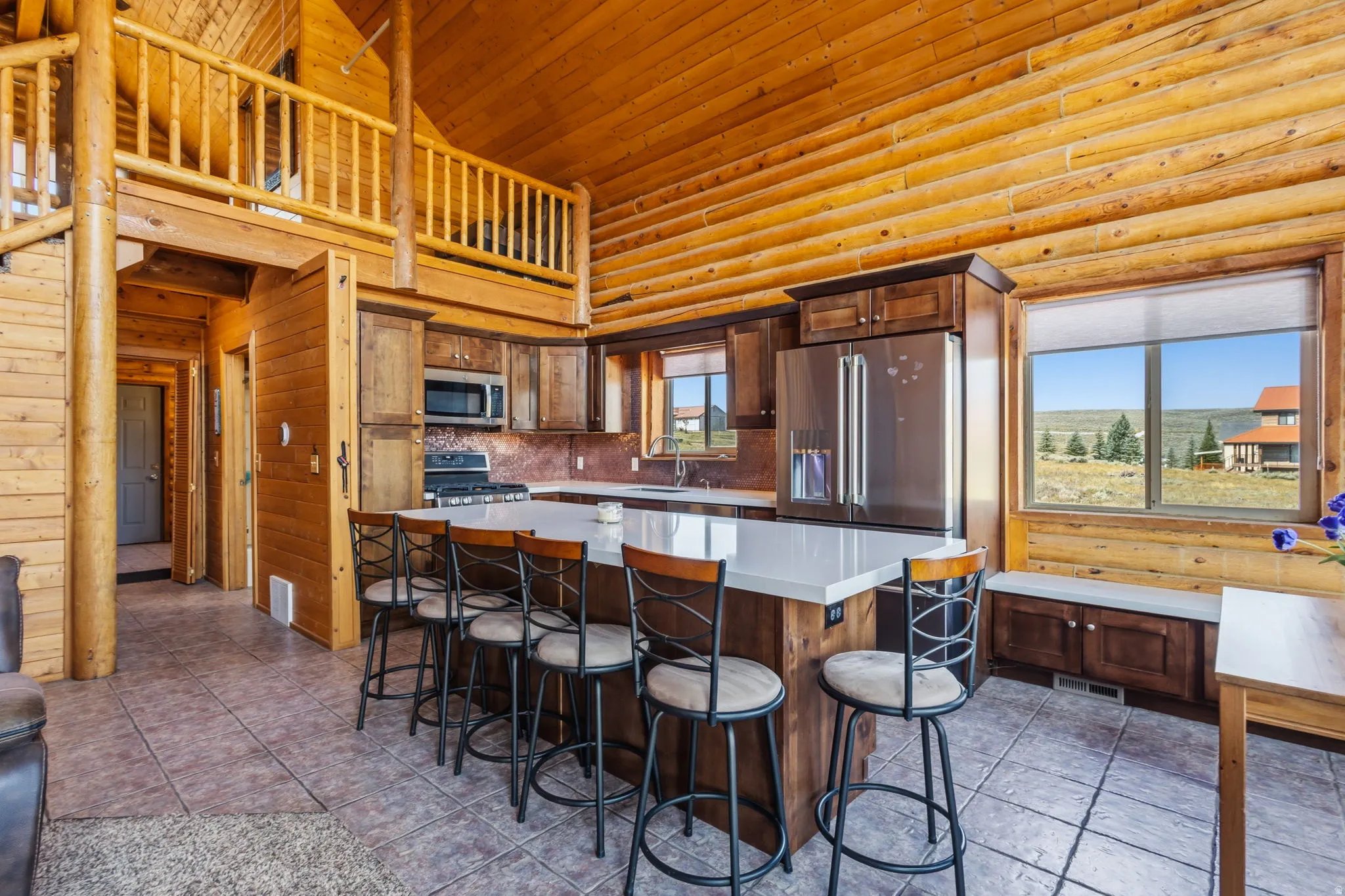 Open-concept kitchen with stainless steel appliances, a large island with seating, dark wood cabinetry, and a window seat with storage