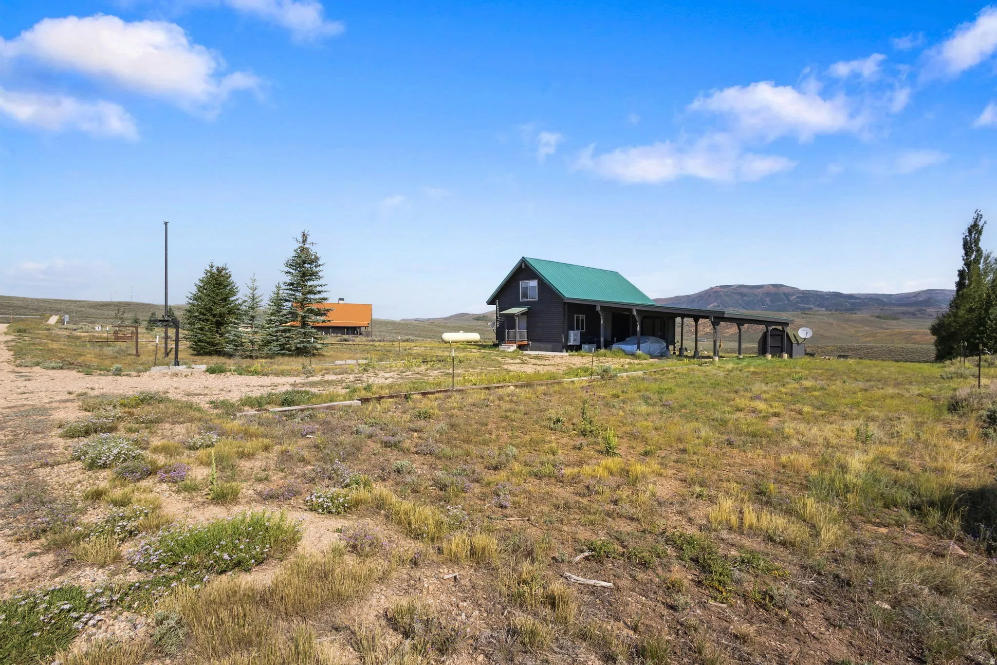 Expansive property featuring a residence with a green metal roof, a covered porch, and a distant mountain backdrop