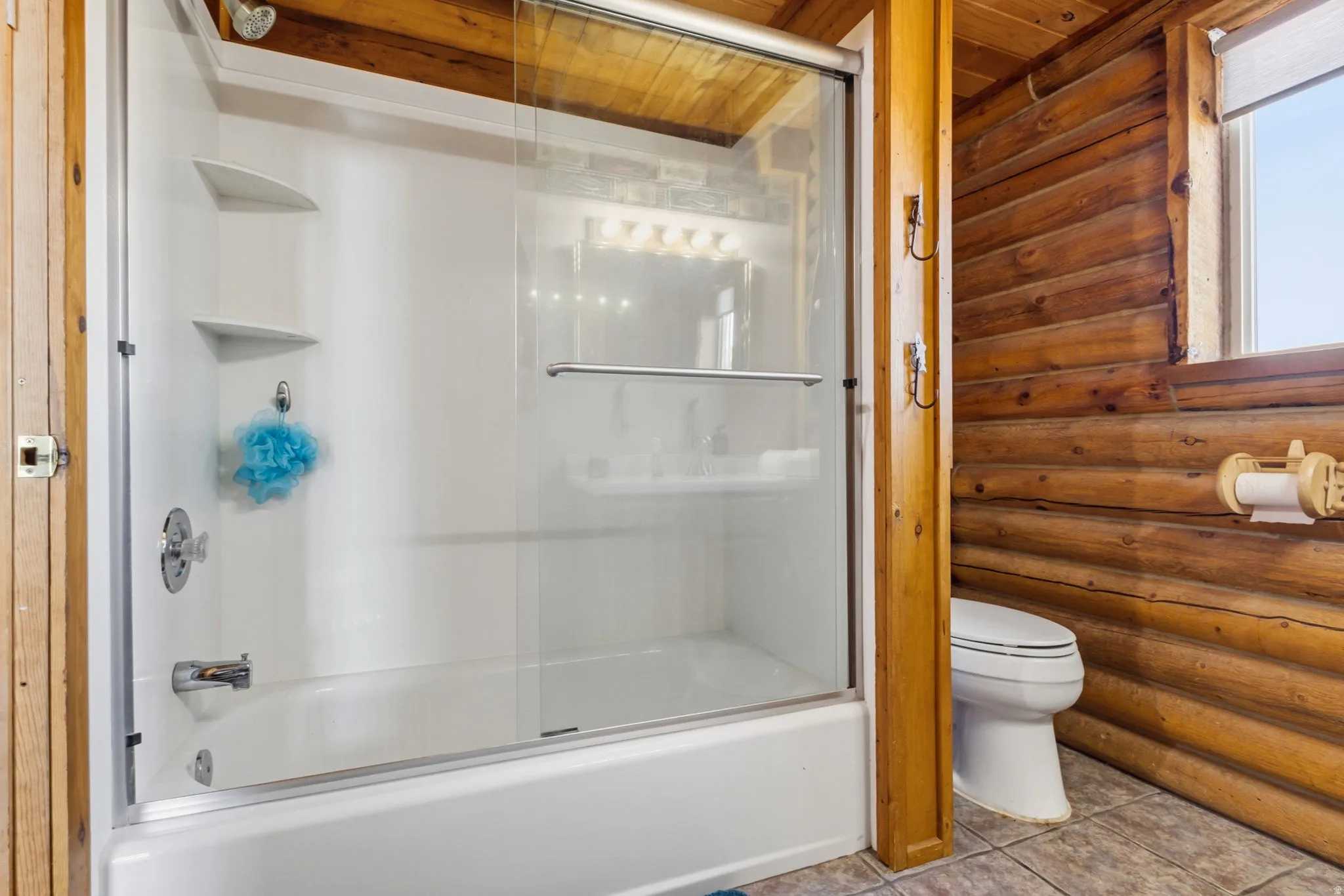Tub and shower combination with sliding glass doors, built-in shelving, and chrome fixtures