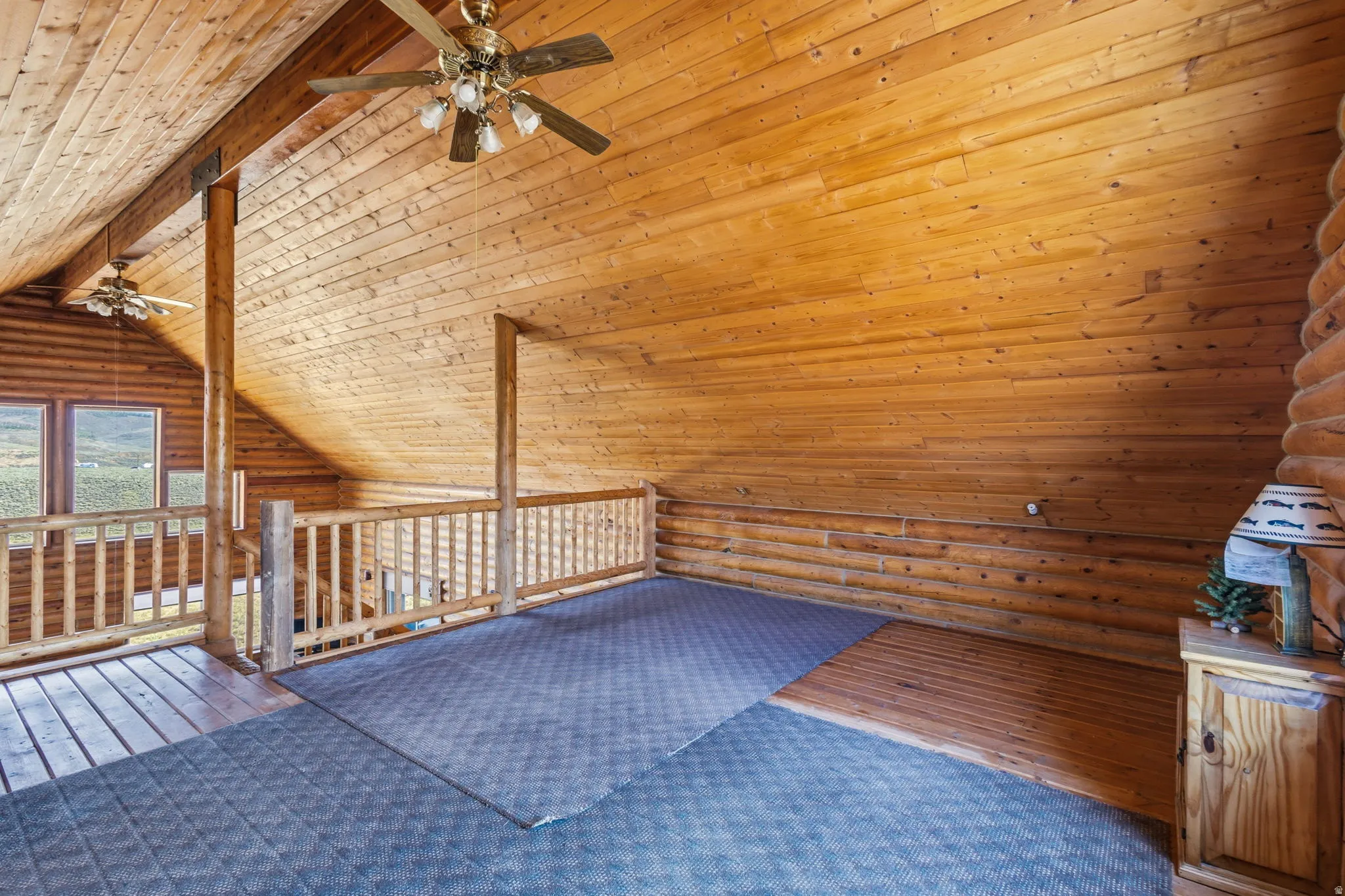 Vaulted wood plank ceiling, exposed wood beams, wood wall paneling, wood railing, and ceiling fans