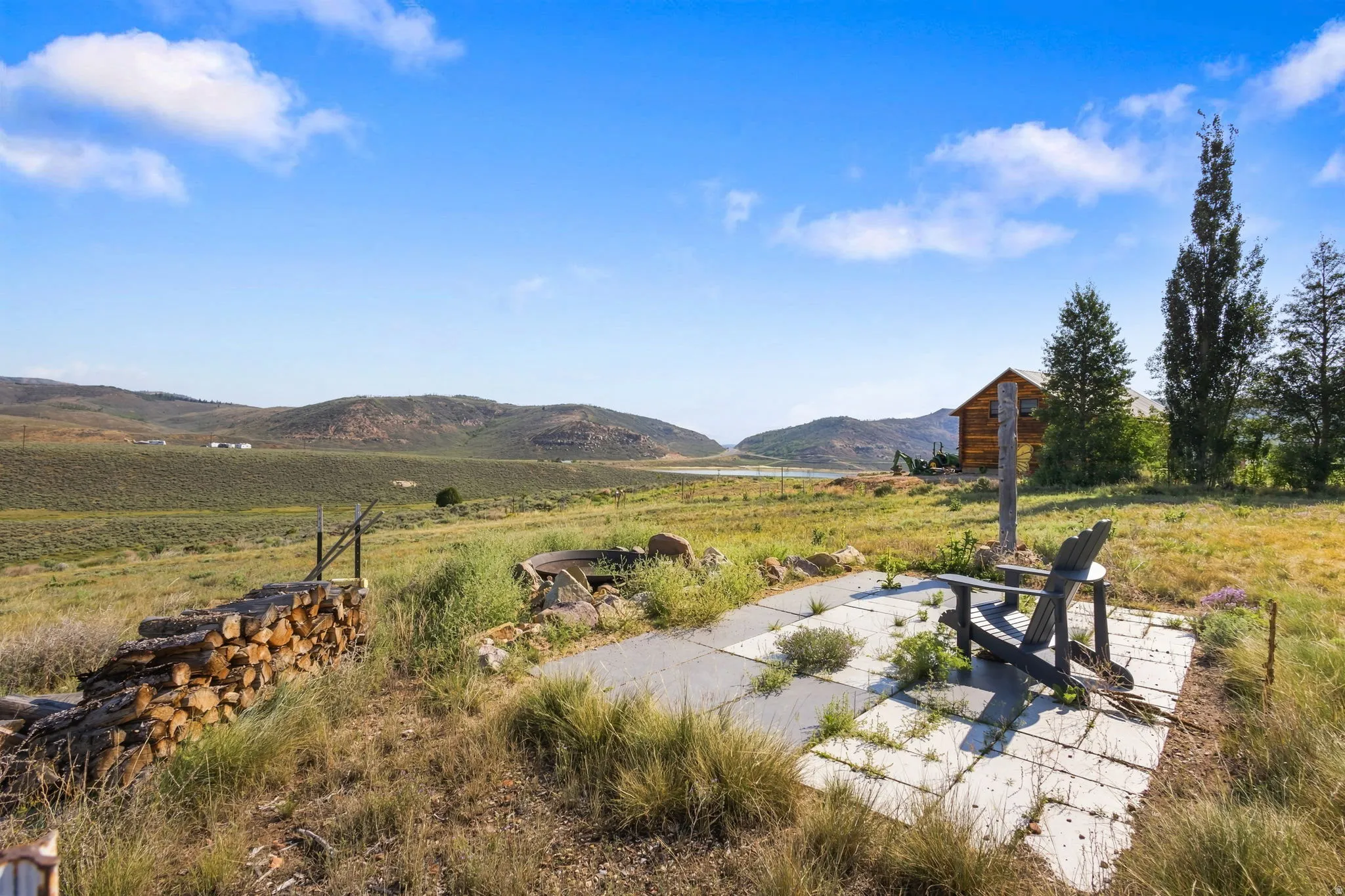 Stone paver patio with natural surroundings, featuring a distant cabin and mature trees