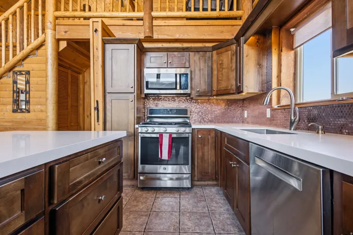 Kitchen featuring stainless steel appliances, wood cabinetry, stone countertops, and a tiled backsplash