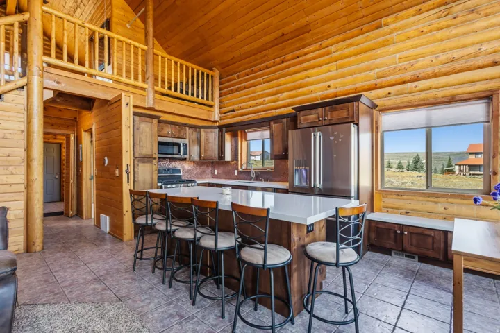 Open-concept kitchen with stainless steel appliances, a large island with seating, dark wood cabinetry, and a window seat with storage