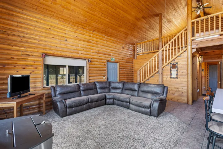Vaulted wood-paneled ceiling, wood-paneled walls, a wood staircase with a wood railing, and a window with a roller shade