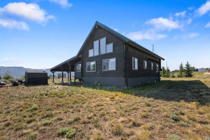 Log cabin exterior with a green metal roof, multiple windows, and a covered porch supported by columns