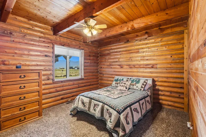 Log wall construction, exposed wood beam ceiling, wood plank ceiling, window with outdoor scenery, ceiling fan with integrated lighting