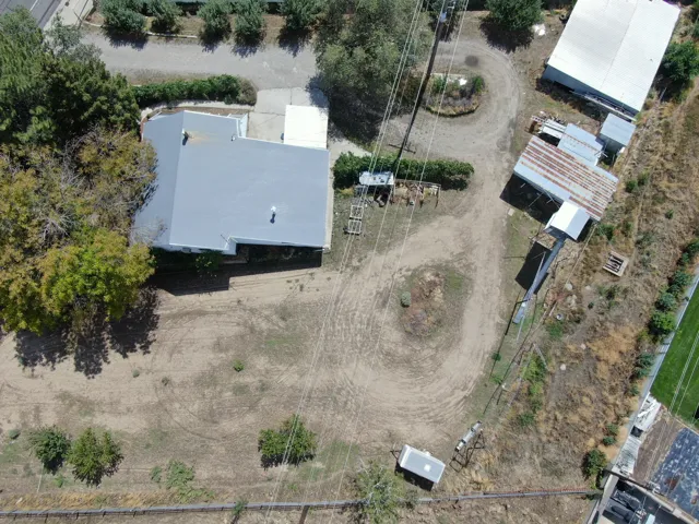 Spacious property featuring a main residence with a light-colored roof, multiple outbuildings, and mature trees