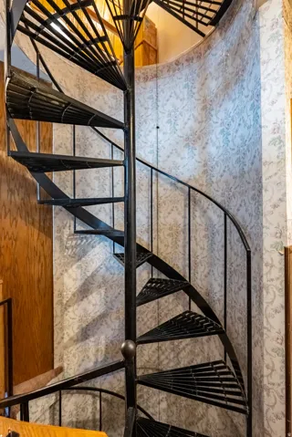 Black spiral staircase with perforated metal treads and a central support column, set against patterned wall covering