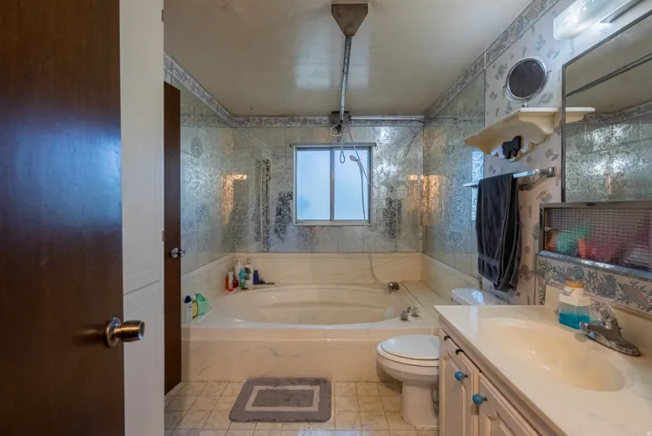 Built-in soaking tub with a window, vanity with an integrated sink, and wall-mounted mirror