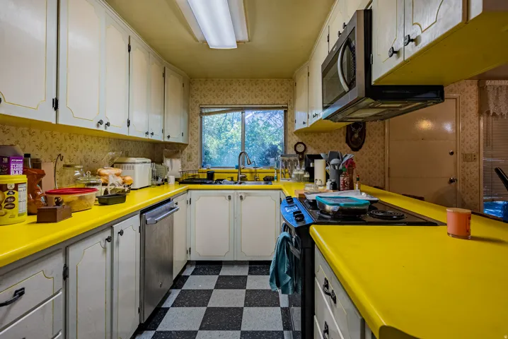 Galley kitchen with checkerboard flooring, a window above the sink, white cabinetry with black hardware, and a built-in microwave