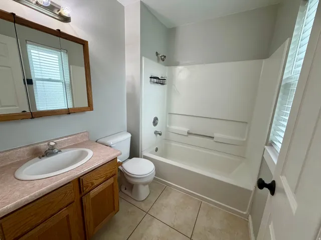 Bathroom featuring a wood-finish vanity with an integrated sink, a built-in medicine cabinet, a full bathtub with shower, and tile flooring
