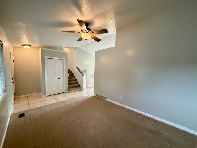 Carpeted flooring, ceiling fan, flush-mount lighting, tiled entry, and staircase with wood handrail