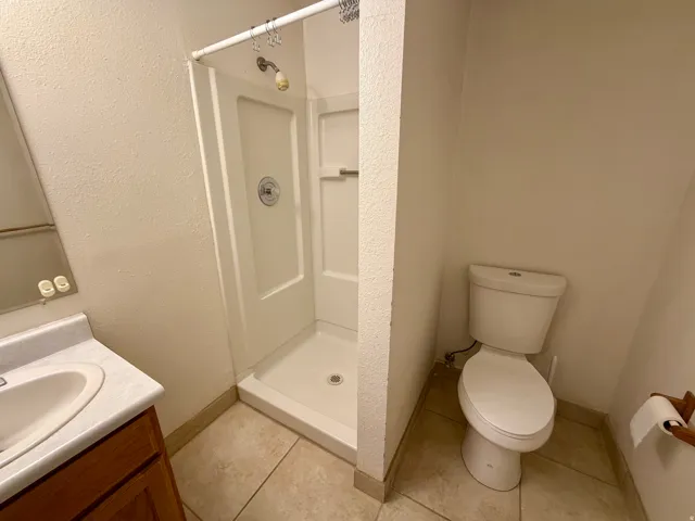 bathroom featuring a single vanity with an integrated sink, a white shower stall with a chrome showerhead, a toilet, and neutral-toned tiled flooring