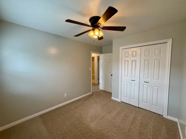 Neutral tone walls with a textured carpeted floor, ceiling fan with integrated lighting, and white bi-fold closet doors