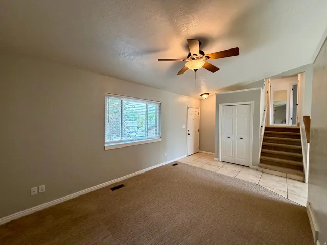 Carpeted living area with a window, ceiling fan, and tiled entry