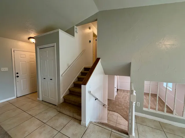 Tiled entry flooring, contrasting wood-finish stair rail, carpeted stairs, and textured wall finishes