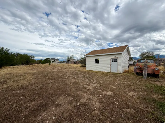 Expansive open lot featuring a detached storage shed with white siding, a white door with lites, and a brown shingle roof