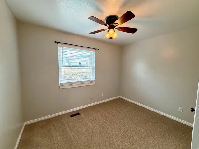 Bright secondary bedroom featuring neutral wall finishes, carpet flooring, a ceiling fan with integrated lighting fixture, and a large window with horizontal blinds providing natural light