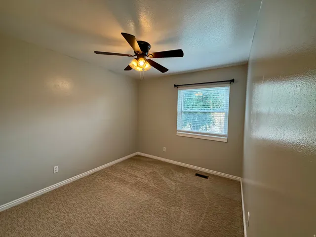 Neutral tone walls, ceiling fan with light fixture, carpeted flooring, and a window with blinds