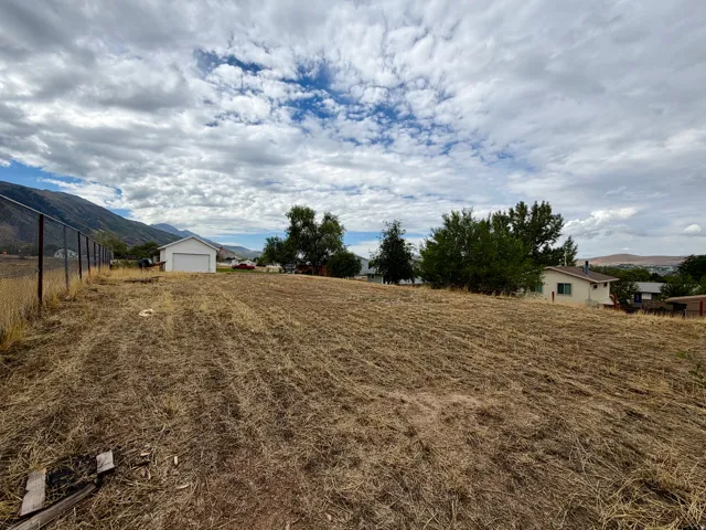 Expansive sloped land featuring a chain-link fence, a white detached garage, and distant mountain scenery