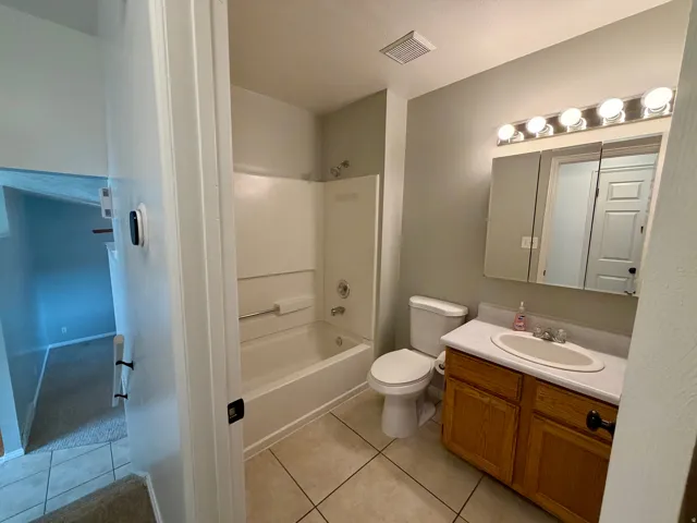 Full bathroom featuring a white bathtub and shower combination, a single vanity with wood-finish cabinetry, a white countertop, and a mirrored medicine cabinet with overhead lighting