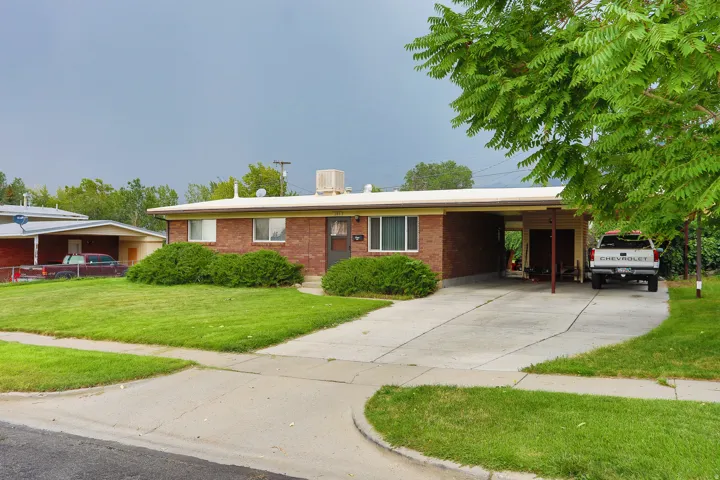 Brick exterior with a covered carport, mature front yard landscaping, and an extended driveway