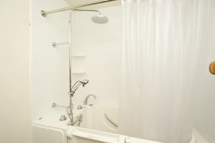 Walk-in tub with built-in grab bars, polished chrome fixtures, and a handheld showerhead
