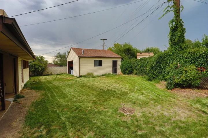 Expansive lawn space featuring a separate utility building with siding and a shingle roof