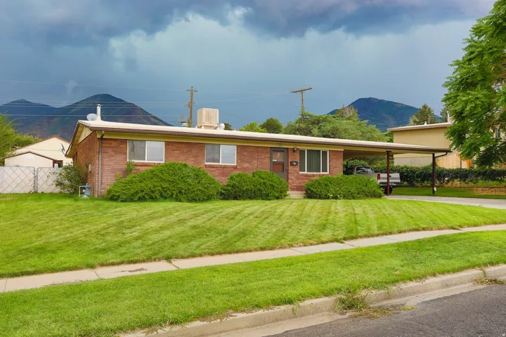 Brick exterior with a covered carport, front yard, and mature landscaping
