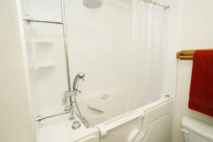 Walk-in tub with built-in grab bars, integrated wall shelving, and a rain showerhead with an adjustable handheld spray
